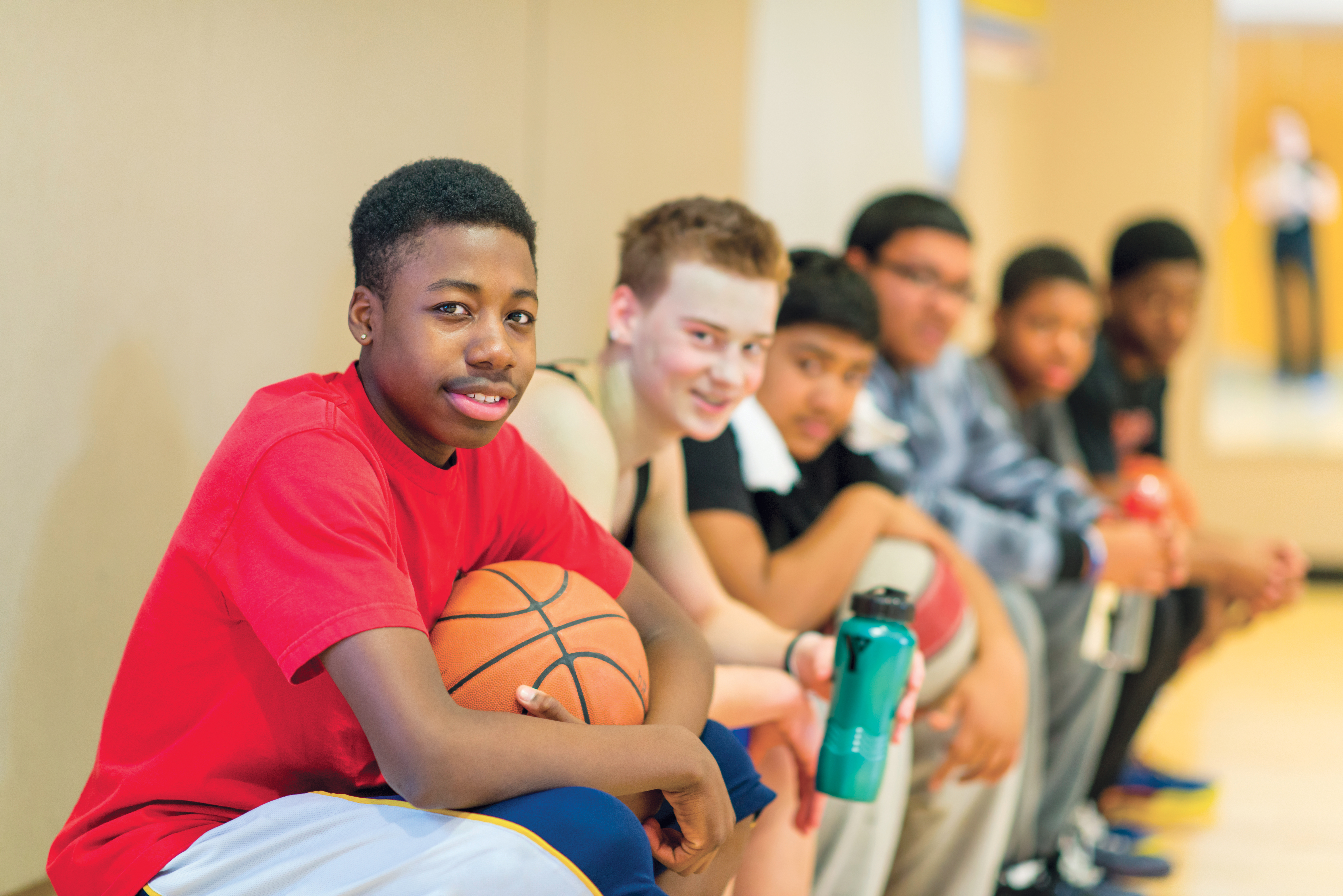 Group of boys sitting on a bench in the gym, posing with a basketball