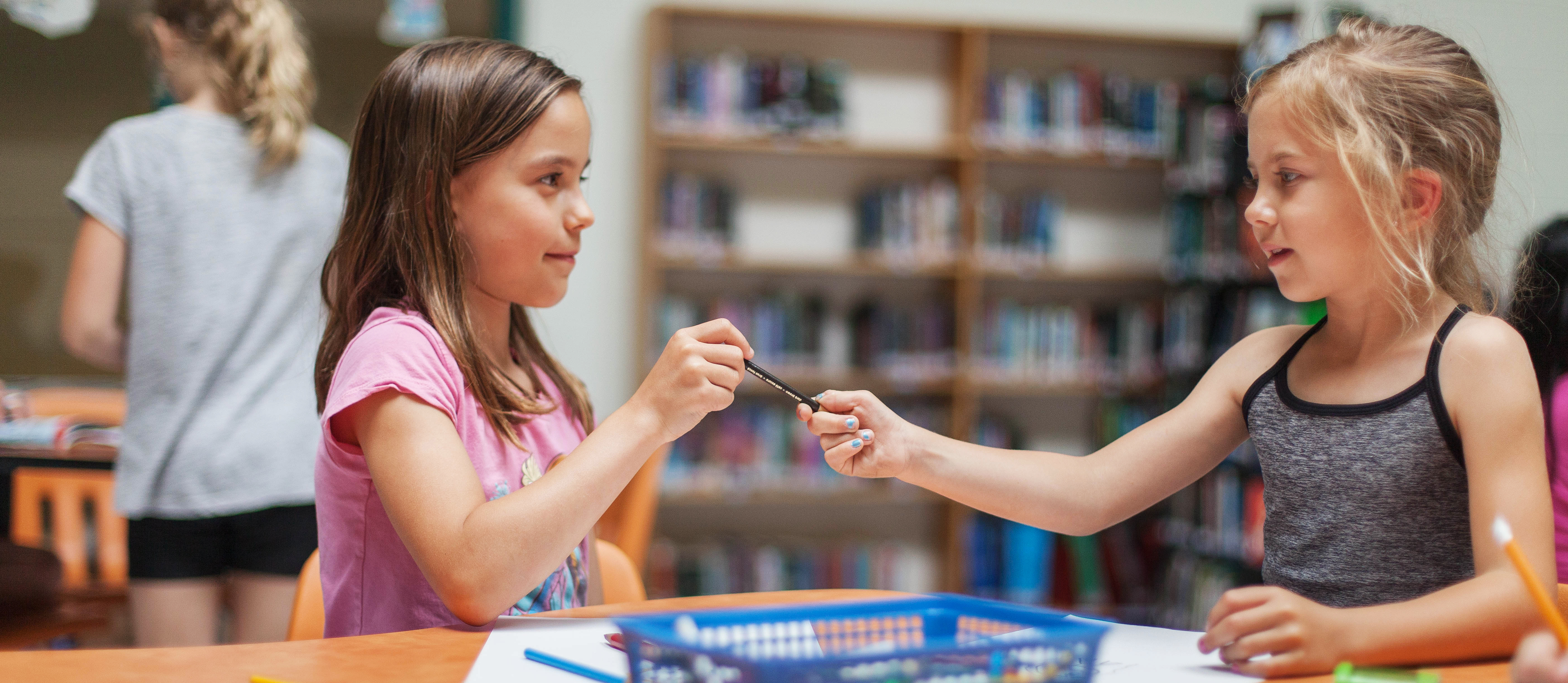 Two girls colouring and sharing a pencil crayon