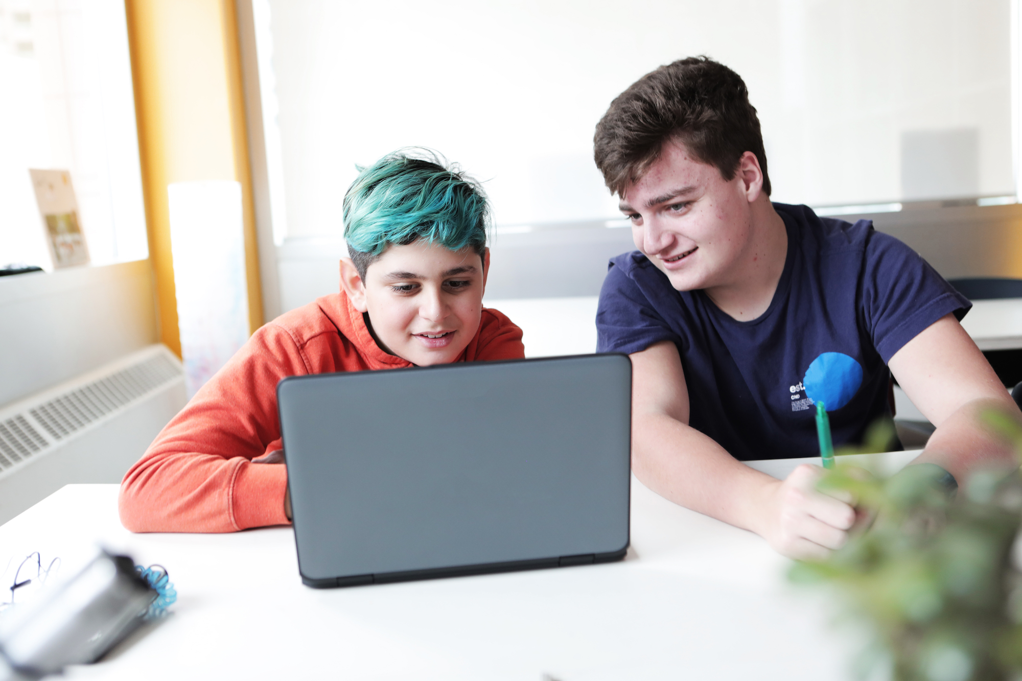 Two teenage boys watch something on a laptop.