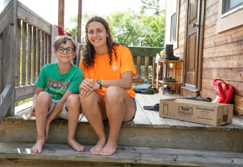 A counsellor and camper smile and sit together on a wooden deck.