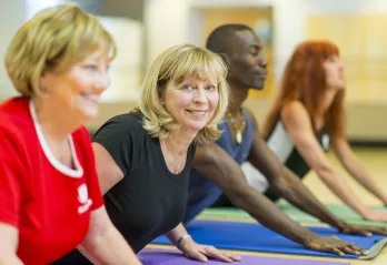 Two older blonde women participate in a group yoga class.