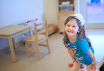 A young girl in a blue tshirt and white flower headband smiles for the camera at a YMCA Child Care Centre.