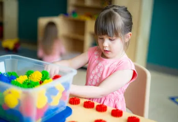 A young girl wearing a pink flower shirt plays with building toys at a table in a YMCA child care centre.