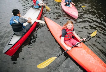 A group of kids paddle on the lake in canoes and kayaks.
