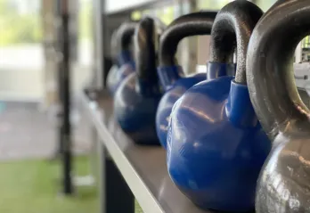 A row of blue and grey kettlebells sits in the turf fitness zone area of a YMCA.