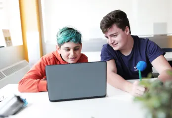 Two teenage boys watch something on a laptop.