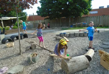 A group of four children explore a YMCA outdoor play space during the summer.