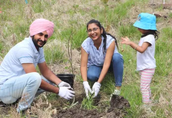 A newcomer family of three laugh and plant a tree together.