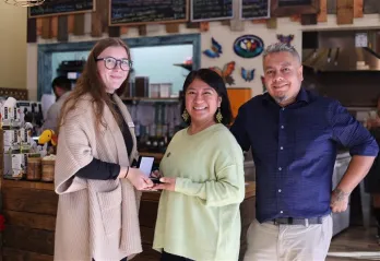 Group of three people standing together, one woman is presenting a medal to another. 
