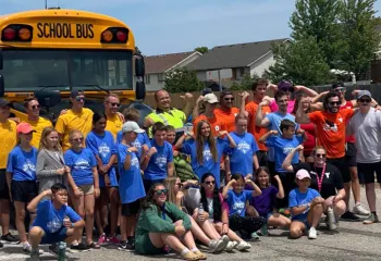 Participants of "Push The Bus" at the Jerry McCaw Family YMCA in Sarnia smile and pose in front of a school bus.