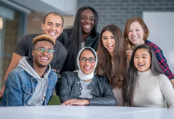 A diverse group of post-secondary students smile around a table.