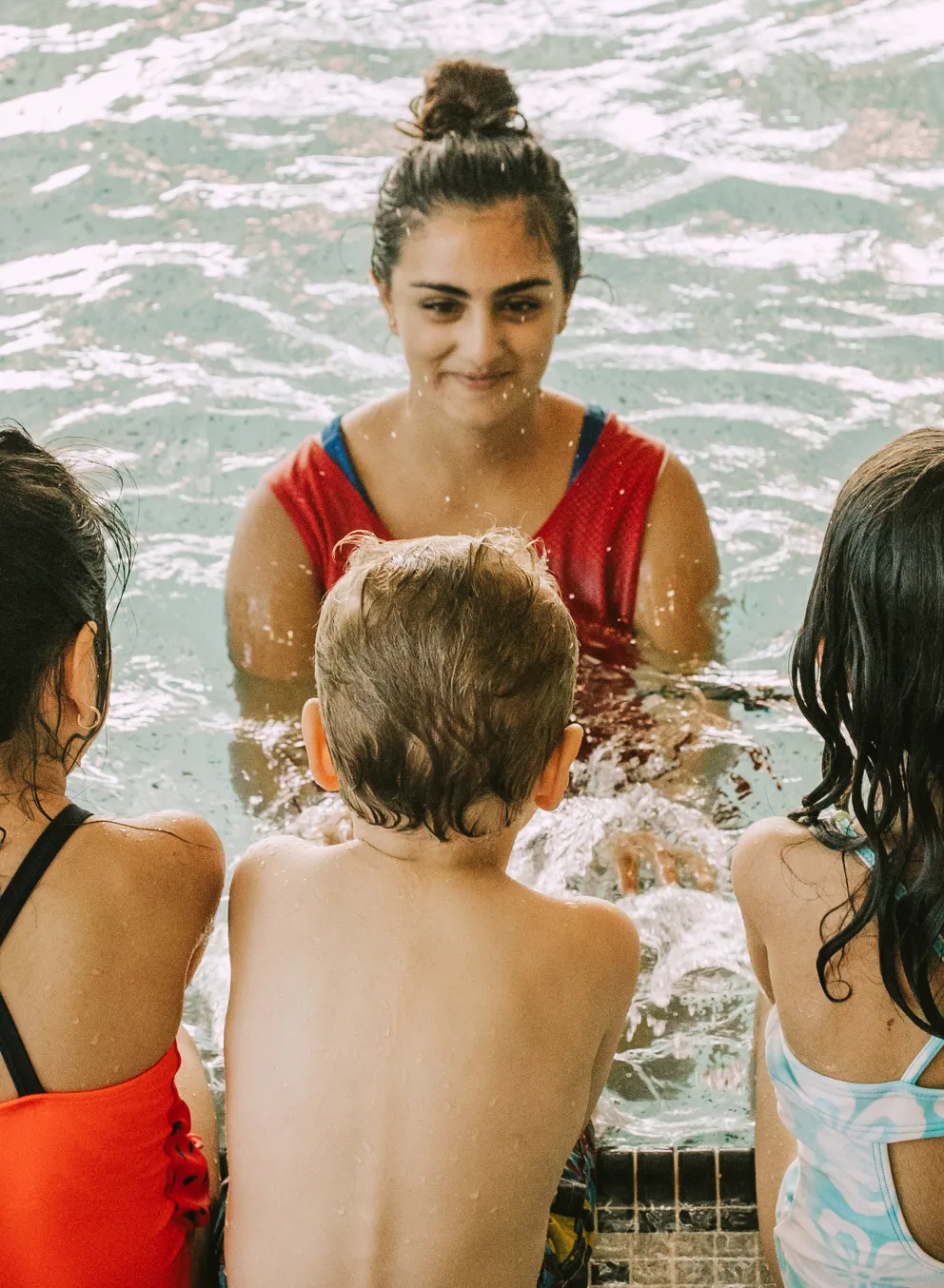 Kids sitting on the pool ledge while the swim instructor talks in the pool