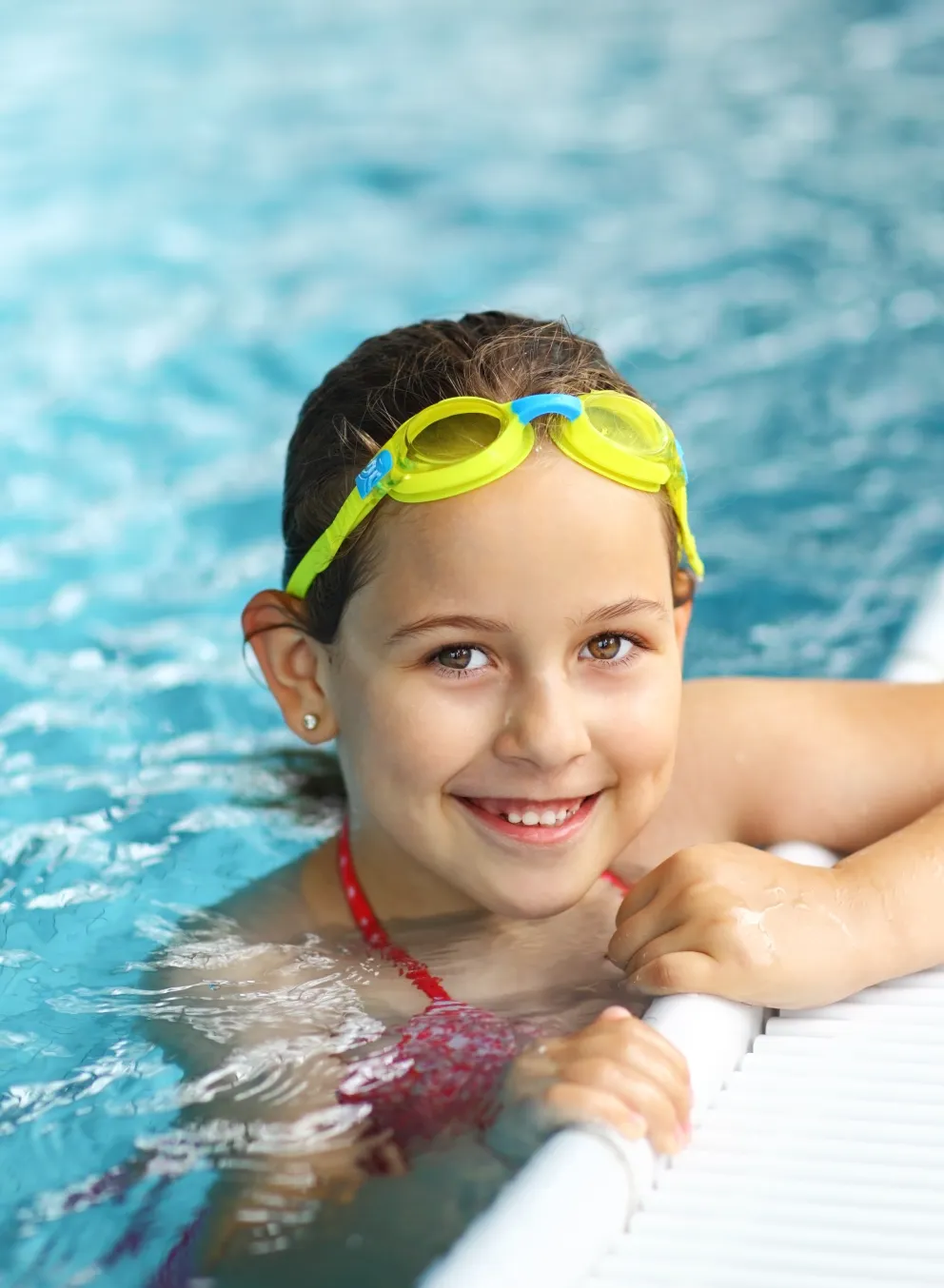 Girl holding onto the edge of the pool smiling.