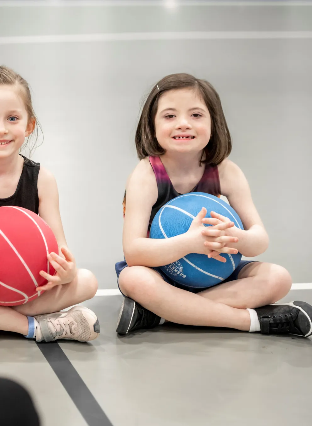 Two girls sitting with basketballs