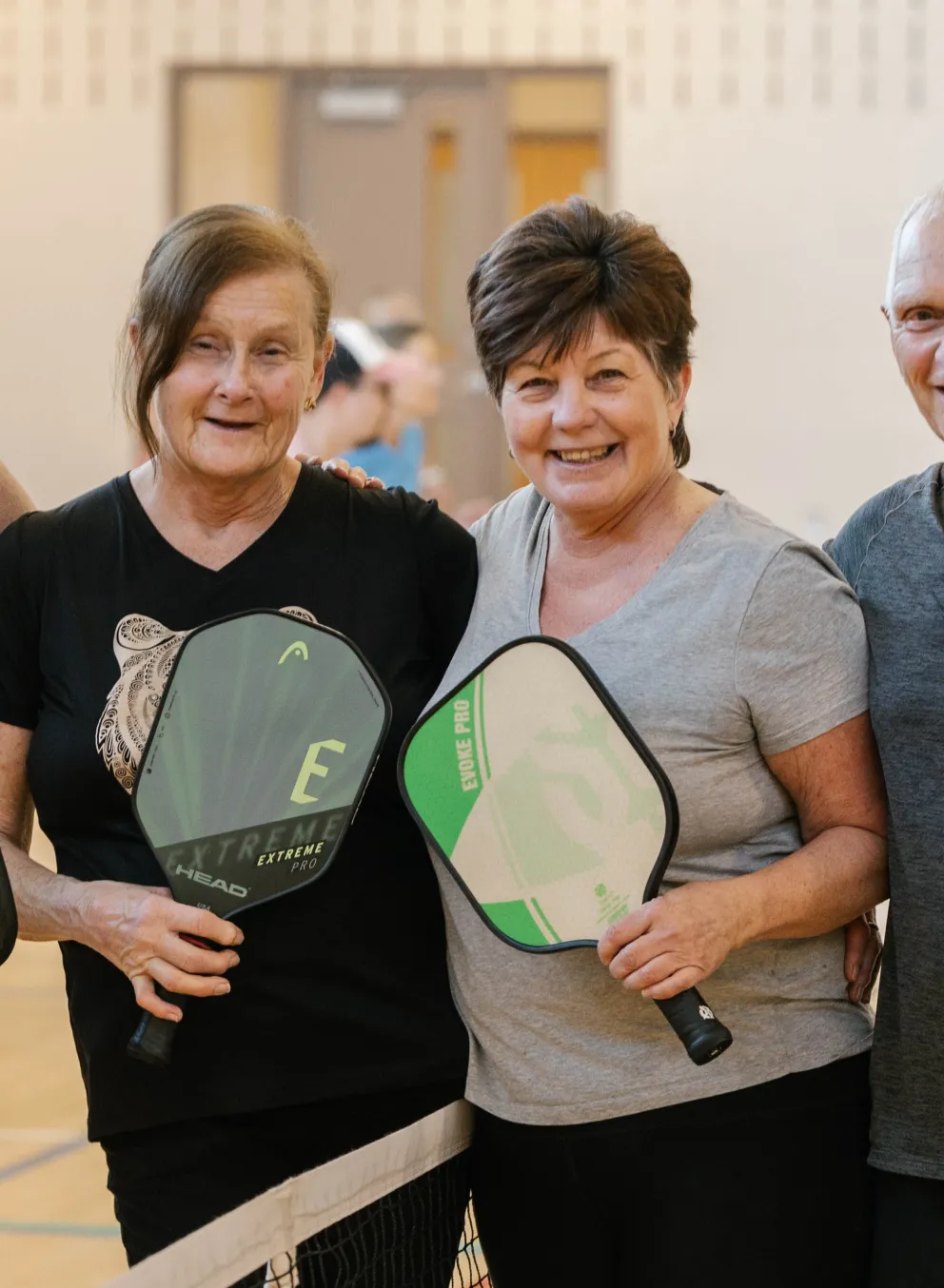 Four adults smiling at pickleball net