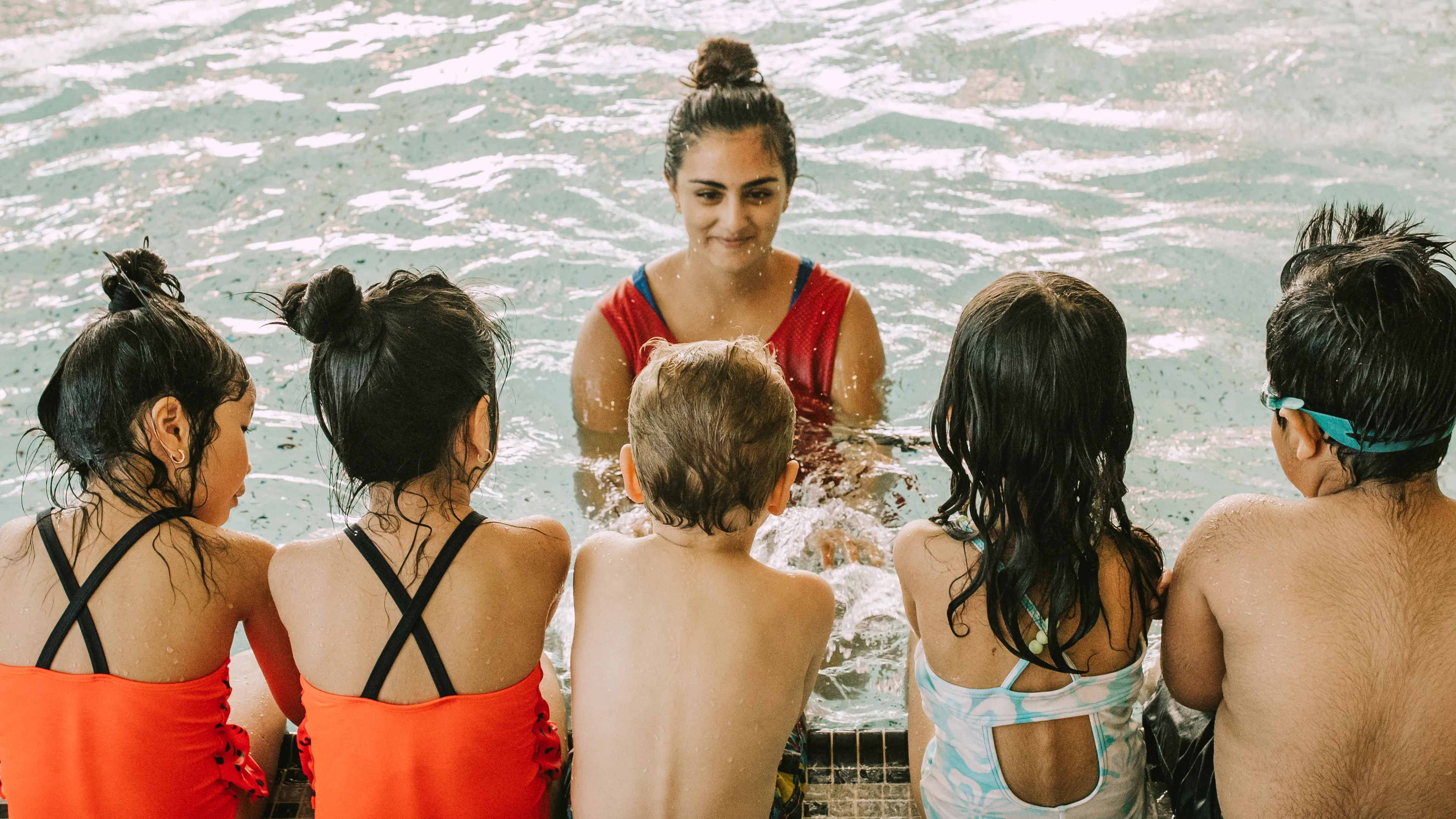Kids sitting on the pool ledge while the swim instructor talks in the pool