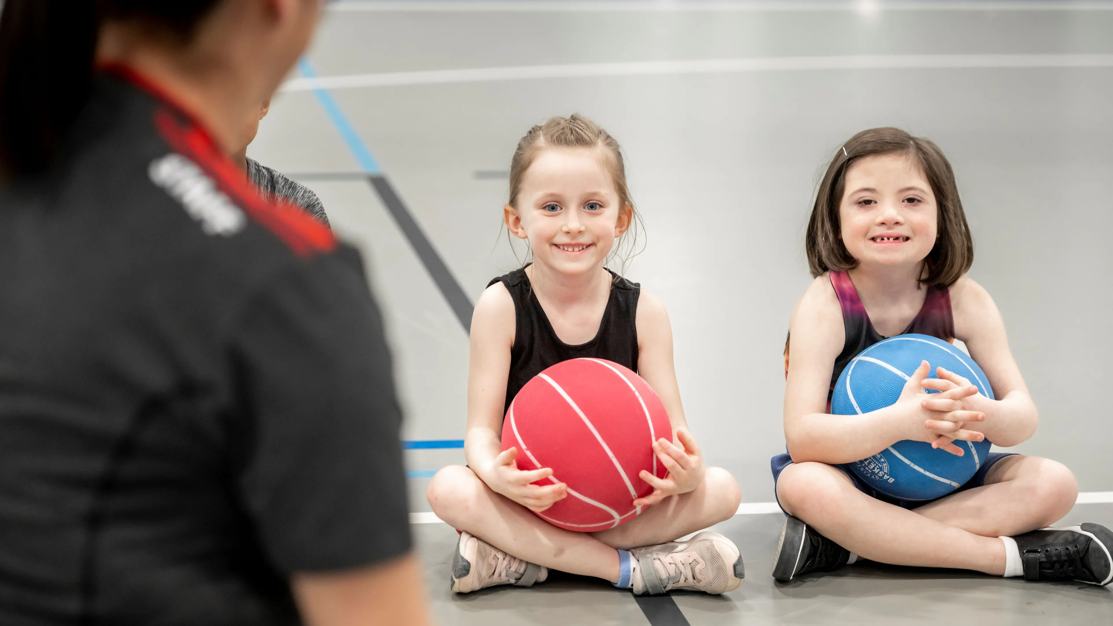 Two girls sitting with basketballs