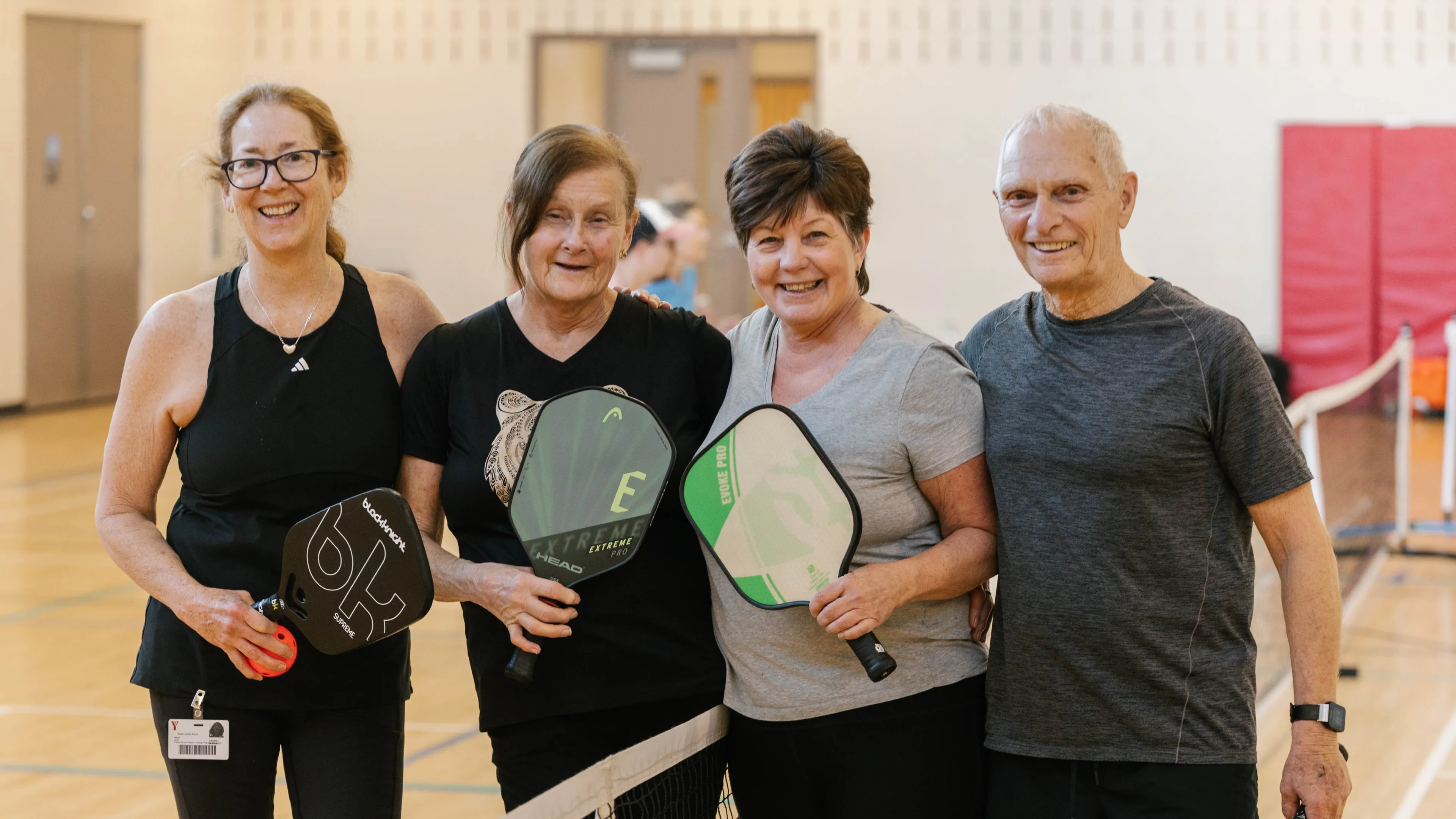 Four adults smiling at pickleball net