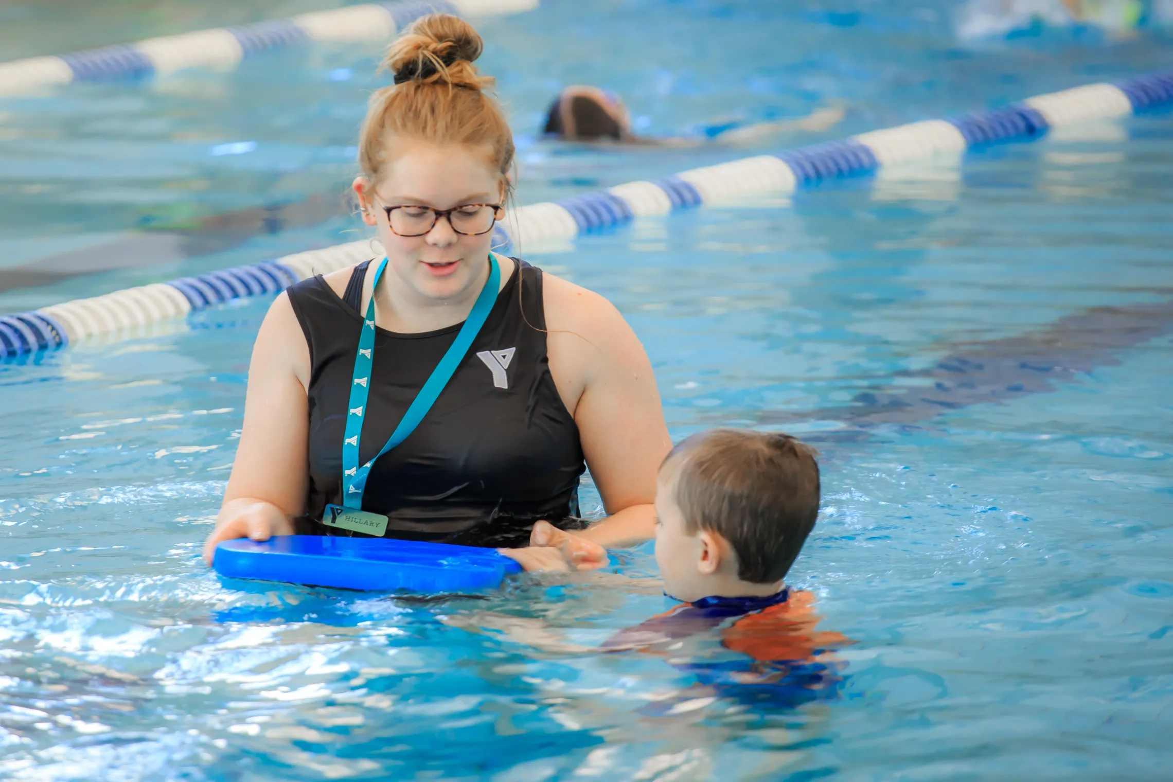 A YMCA lifeguard teaches a boy how to hold a flutter board in a Y facility pool.