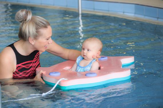 A young mother holds her infant in a flotation device in a Y pool.