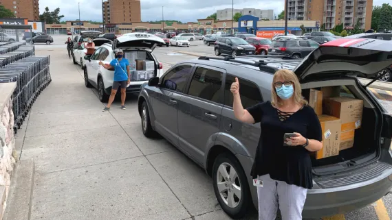 YMCA staff pick up items for Kids Club kits with a distanced line of cars.