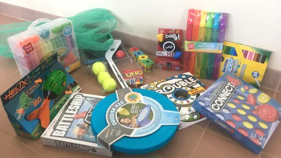A collection of items for the family game bag: Helix football, Play Doh, Battleship, tennis balls, Ogodisk, Uno, Trouble, Connect 4, Crayola markers, Bubbles, Bop-it!