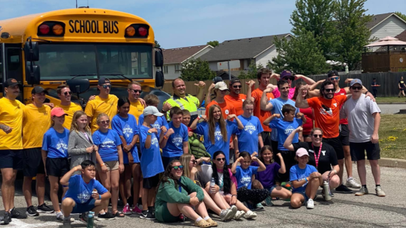 Participants of "Push The Bus" at the Jerry McCaw Family YMCA in Sarnia smile and pose in front of a school bus.
