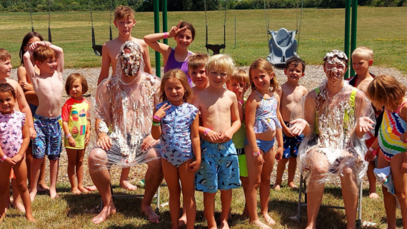 A group of children at camp laugh with Y staff in plastic ponchos, covered with pie at Petrolia YMCA's "Pie in the Face" fundraiser.