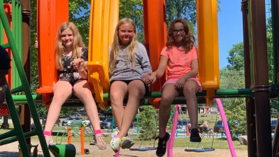 Three girls hold hands and smile on a playground at day camp in St. Thomas.