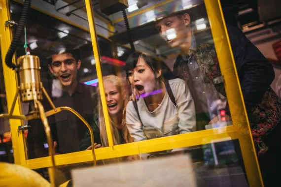 A group of teens excitedly plays a claw machine game.