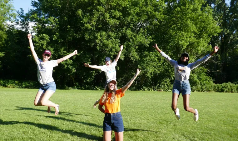 The YMCA Overnight Camp team jump and smile in a grassy field.