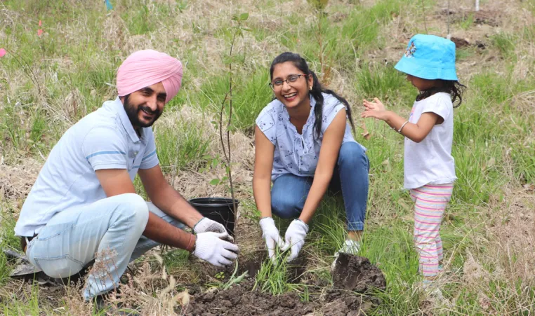 A newcomer family of three laugh and plant a tree together.