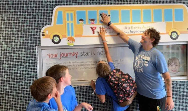 Three kids help a Y staff member update the Fill The Bus tracker at the Chatham YMCA.