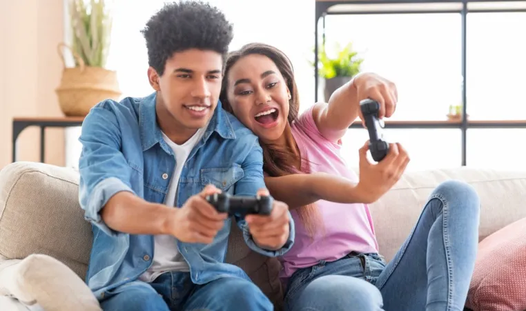 Two teens excitedly play video games on a couch.