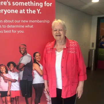 Barb smiles in front of a YMCA pop-up sign wearing a red shirt and black pants.