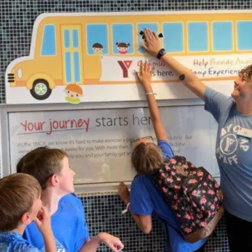 Three kids help a Y staff member update the Fill The Bus tracker at the Chatham YMCA.