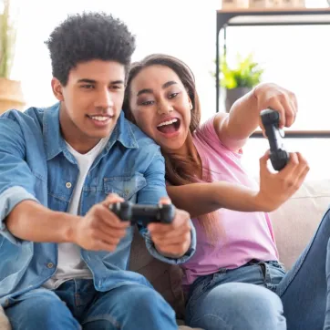 Two teens excitedly play video games on a couch.