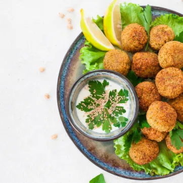 A blue bowl of falafels on a bed of lettuce with a side sauce.