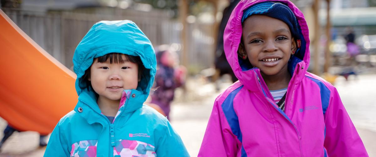 Two girls in bright spring coats, stay bundled while playing outside.