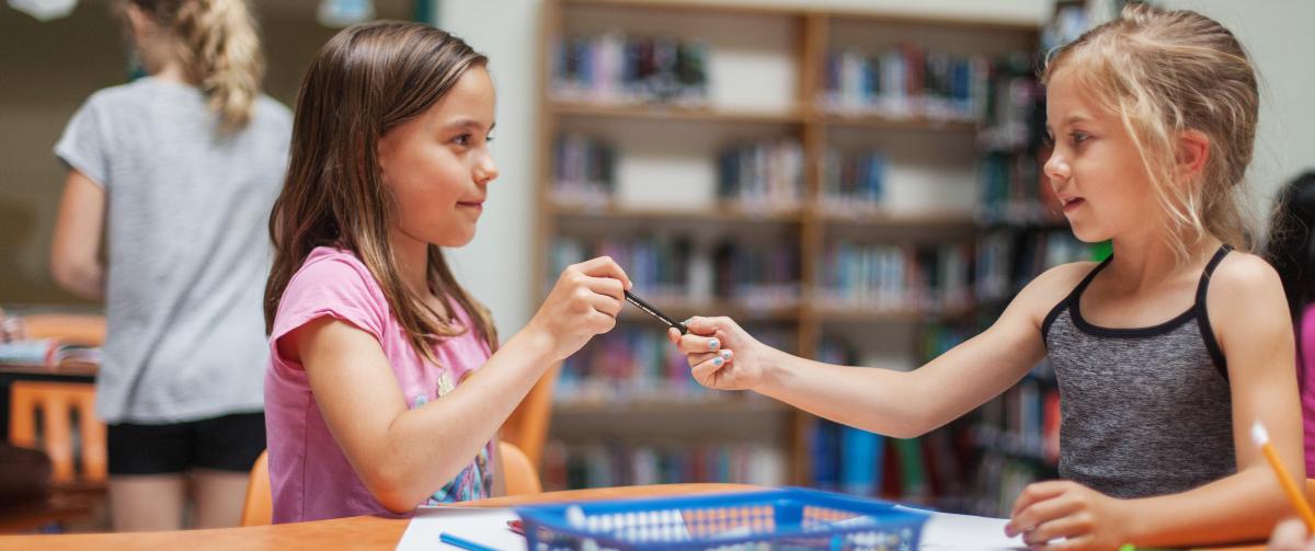 Two girls colouring, sharing pencil crayons
