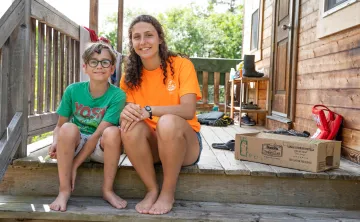 A counsellor and camper smile and sit together on a wooden deck.
