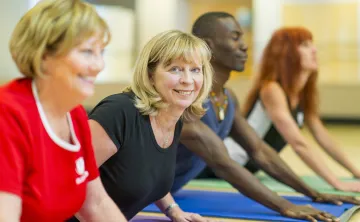 Two older blonde women participate in a group yoga class.