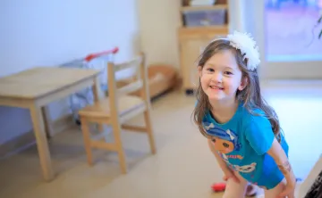 A young girl in a blue tshirt and white flower headband smiles for the camera at a YMCA Child Care Centre.