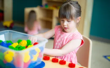 A young girl wearing a pink flower shirt plays with building toys at a table in a YMCA child care centre.