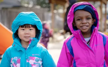 Two girls in bright spring coats, stay bundled while playing outside.