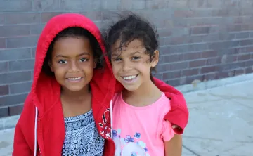 A girl in a red hoodie puts her arm around her friend in a pink t-shirt at YMCA Day Camp.