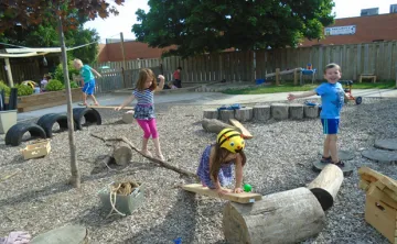 A group of four children explore a YMCA outdoor play space during the summer.