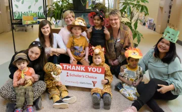 YMCA Staff pose with children from a Y Child Care Centre in costumes, holding a sign thanking Scholar's Choice for their sponsorship of Move-A-Thon.