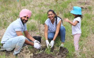 A newcomer family of three laugh and plant a tree together.