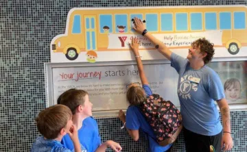 Three kids help a Y staff member update the Fill The Bus tracker at the Chatham YMCA.